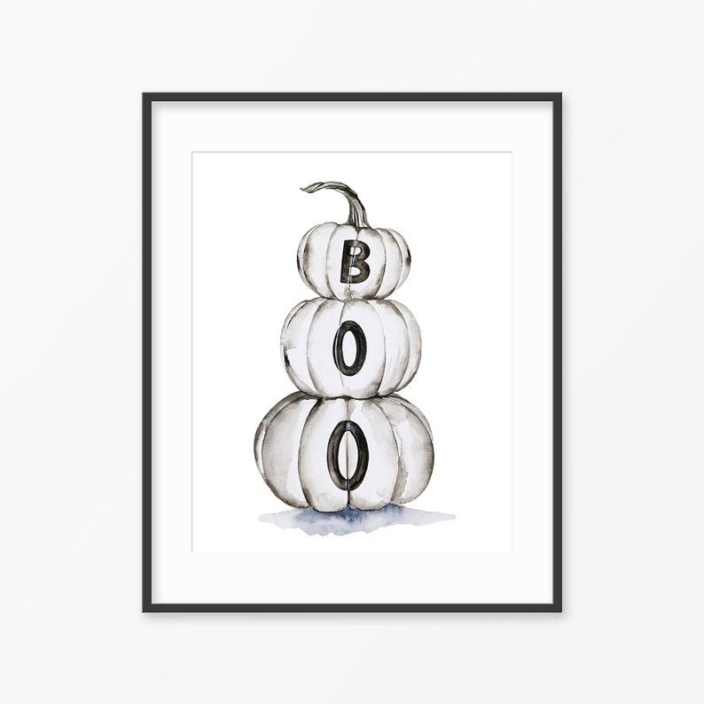 Op de afbeelding: Een stapel van drie witte pompoenen met het woord "BOO" erop geschreven in zwarte letters. De pompoenen zijn op elkaar gestapeld, met de grootste pompoen onderaan en de kleinste pompoen bovenaan.