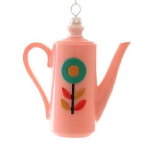 Puede incluir: Adorno de Navidad de cerámica rosa en forma de tetera con un diseño de flor estilizado en tonos de verde, naranja y rojo.