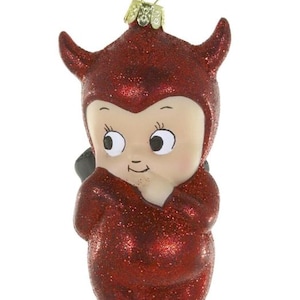 Op de afbeelding: Een hangend ornament in de vorm van een klein figuurtje in een rood glitterend duivelskostuum met hoorns. Het figuurtje heeft een bleek gezicht, grote ogen en een hand bij de mond. Het is voorzien van een goudkleurige metalen dop en koord.