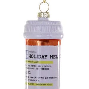 May include: A Christmas tree ornament in the shape of a pill bottle. The ornament is white and orange with the text "HOLIDAY HELP" and "HOLIDAY-SANITY". It has a gold-coloured string for hanging.