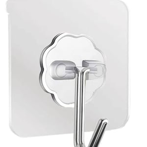 May include: A clear plastic adhesive hook with a silver metal hook. The hook is designed to be mounted on a wall or other smooth surface.