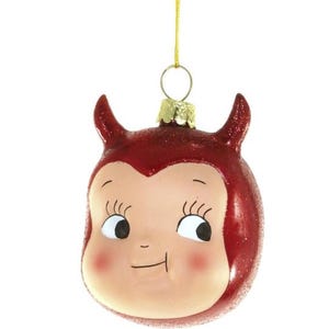 以下が含まれることがあります： 赤いグリッター仕上げの悪魔をモチーフにしたクリスマスオーナメント。青白い顔にバラ色の頬、長いまつげの大きな目、小さな笑みを浮かべています。頭部には2本の小さな角があり、金色のキャップに取り付けられた細い金色の紐で吊り下げられています。
