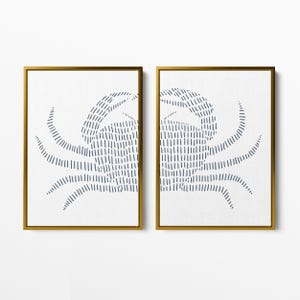 May include: A set of two framed prints featuring a stylized blue crab design on a white background. The frames are gold.