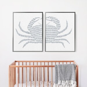 May include: Two framed prints of a blue crab design. The crab is made up of a series of thin, vertical lines. The prints are hung on a white wall above a wooden crib.