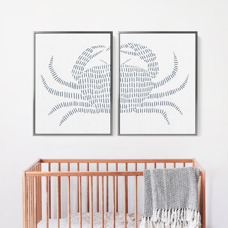 May include: Two framed prints of a blue crab design. The crab is made up of a series of thin, vertical lines. The prints are hung on a white wall above a wooden crib.