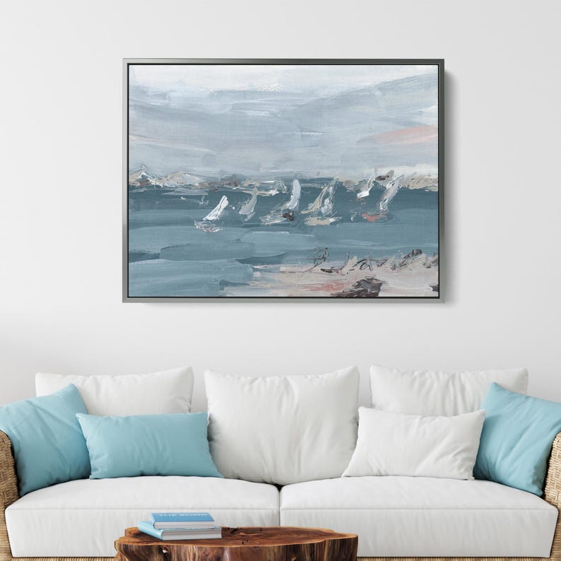 May include: Abstract painting of a seascape with sailboats in the distance. The painting is done in shades of blue, grey, and white, with a hint of pink in the sky. The painting is framed in a silver frame.