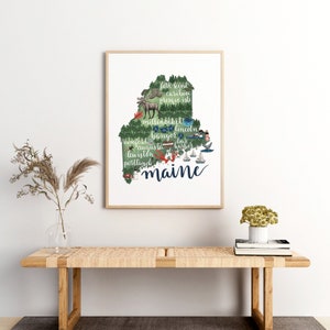 May include: A print of the state of Maine with the names of cities and towns throughout the state. The print is in a light wood frame and is hanging on a white wall.