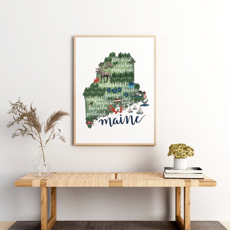 May include: A print of the state of Maine with the names of cities and towns throughout the state. The print is in a light wood frame and is hanging on a white wall.