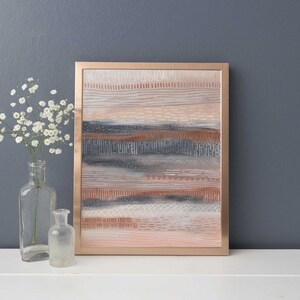 May include: Abstract art print with a copper frame. The print features a layered design of horizontal lines and patterns in shades of pink, brown, gray, and white.