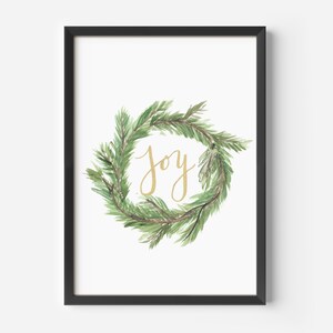 May include: A framed print featuring a watercolor wreath of green pine needles. The word "joy" is written in gold script in the center of the wreath. The frame is black, and the background is white.