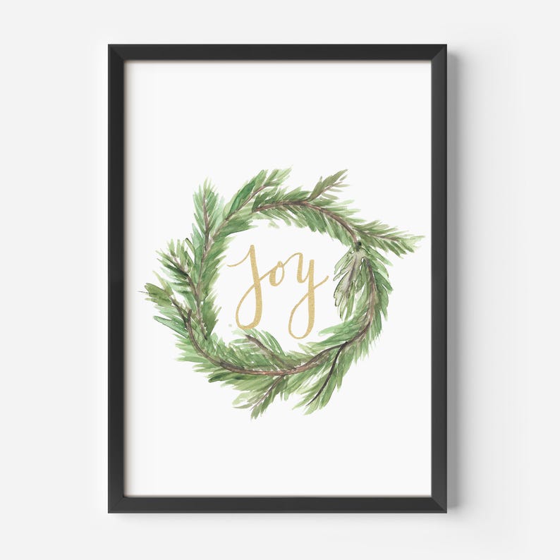 May include: A framed print featuring a watercolor wreath of green pine needles. The word "joy" is written in gold script in the center of the wreath. The frame is black, and the background is white.