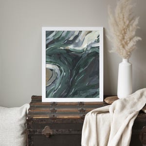 May include: Abstract painting with swirling green, blue, and white colors. The painting is framed in a white frame and is hanging on a wall.
