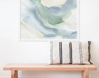 May include: A framed abstract painting with a white frame and a light blue and green color scheme. The painting is hanging on a white wall above a wooden bench with a striped pillow.