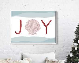 以下が含まれることがあります： 赤い文字で「JOY」と書かれた額入りのアートプリント。中央には赤い貝殻があり、背景には青と白のストライプがあります。白いソファの上に飾られており、海岸をテーマにした作品です。