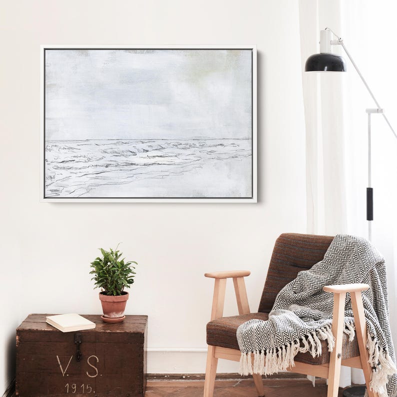 May include: A minimalist abstract painting of a seascape in shades of gray and white. The painting features a horizon line with waves and a sky with subtle hints of green. The painting is framed in a white frame.