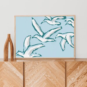 May include: A framed print of a blue and white abstract painting featuring stylized birds in flight against a light blue background.