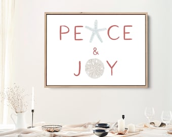 以下が含まれることがあります： 赤い文字で「PEACE & JOY」と書かれた額入りのアートプリント。薄い青色のヒトデが文字「C」を、砂ドルが文字「O」を置き換えています。このアートワークは、木製のテーブルの上にある白い壁に飾られています。