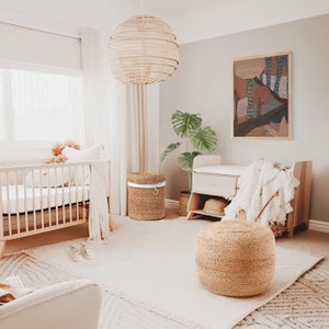 May include: A nursery room with a crib, a changing table, a wicker ottoman, and a woven basket. The walls are painted a light gray and the room is decorated in a neutral color scheme.