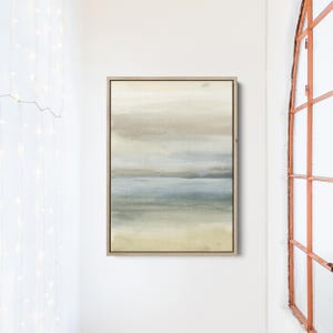 May include: Abstract painting with a muted color palette of beige, gray, and blue. The painting depicts a landscape with a horizon line and a sky with clouds. The painting is framed in a light wood frame.