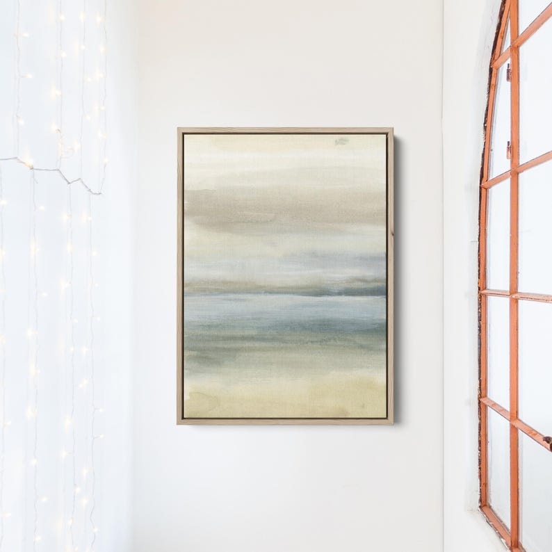 May include: Abstract painting with a muted color palette of beige, gray, and blue. The painting depicts a landscape with a horizon line and a sky with clouds. The painting is framed in a light wood frame.