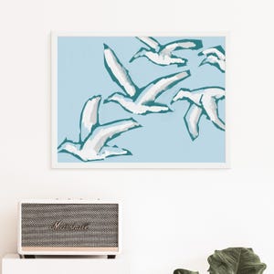 May include: A framed print of a minimalist abstract art design featuring white birds flying against a light blue background. The birds are outlined in teal.