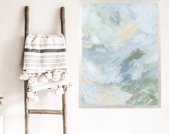 May include: Abstract painting in shades of blue, green, and yellow. The painting is framed in a light wood frame and is hanging on a white wall.