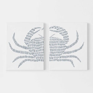 May include: Two white canvases with a blue line drawing of a crab on each. The crab is drawn with a series of short, parallel lines.
