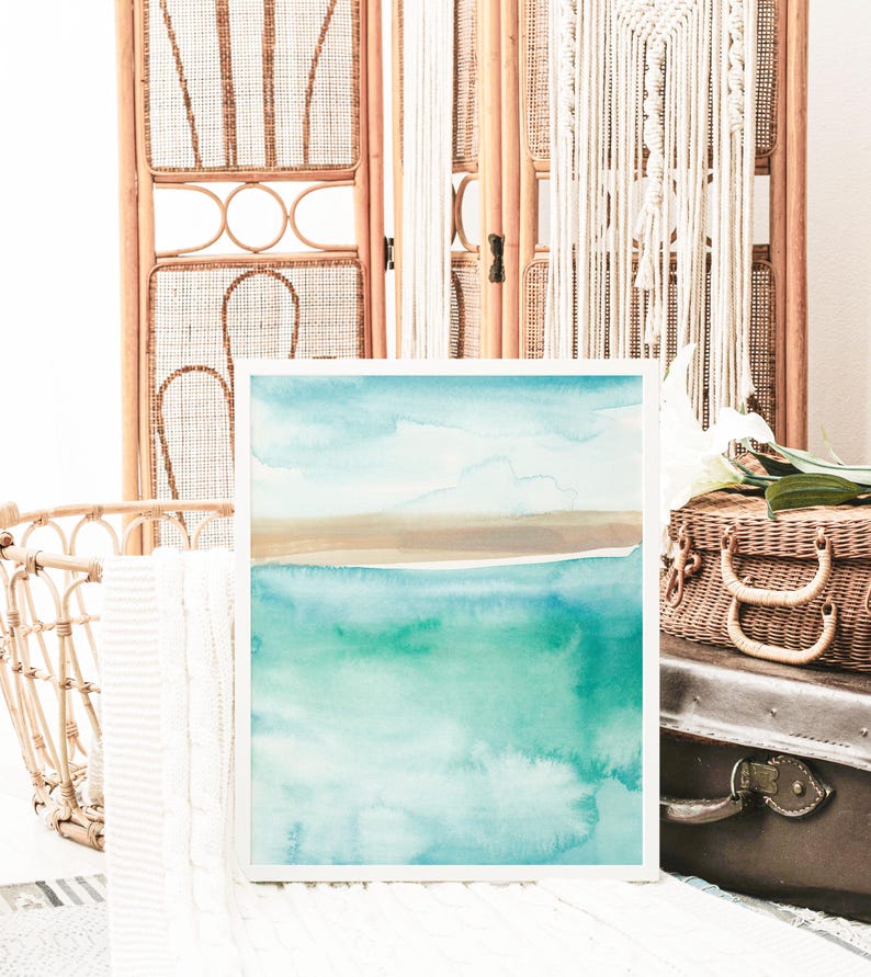 May include: A framed watercolor painting of a seascape with a light blue sky, brown sand, and turquoise water.
