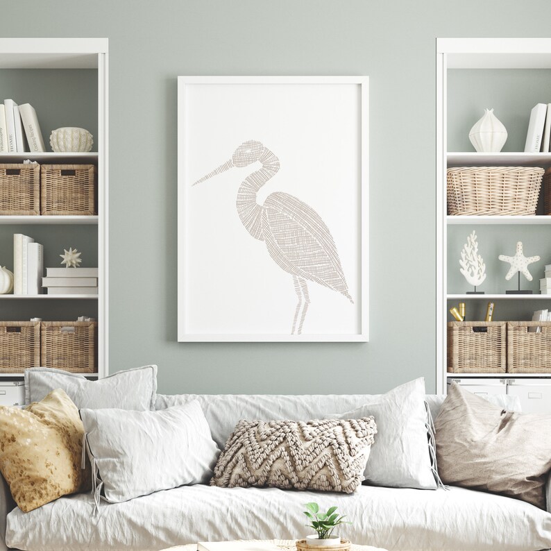 May include: A white framed print of a stylized line drawing of a heron in a light brown color. The print is hanging on a light green wall above a white couch with beige pillows.