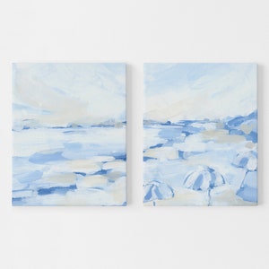 May include: A set of two abstract paintings on canvas. The paintings are in shades of blue and white and depict a seascape with a horizon line and clouds. The right painting also features a few white umbrellas.