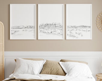 Puede incluir: Tres dibujos en blanco y negro de paisajes en marcos blancos sobre una pared beige encima de una cama con ropa de cama blanca y una manta de color marrón.