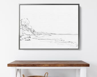 May include: A black and white sketch of a beach scene with trees and a shoreline. The sketch is framed in a silver frame and hanging on a white wall above a wooden table.