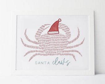 May include: A framed print featuring a red crab wearing a Santa hat. The crab is drawn with vertical lines, and the text "SANTA claws" is below in a light blue script font. The print is in a white frame.