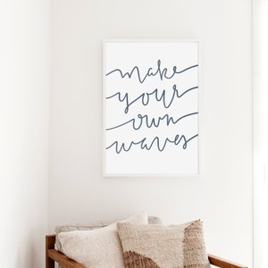 May include: A white framed print with the text "make your own waves" in blue cursive script.