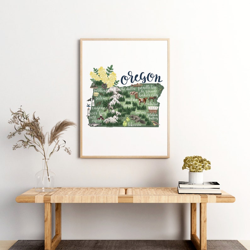 May include: A green and brown illustrated map of Oregon with the state name in blue cursive lettering. The map includes various cities and towns throughout the state, along with small illustrations of animals, plants, and landmarks.