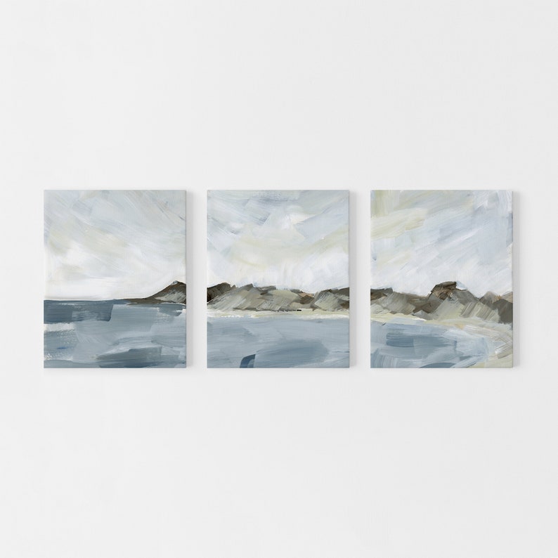 May include: Set of three abstract landscape paintings. Each canvas features a serene scene with a blue body of water, a brown and gray landmass, and a light blue and white sky. The artwork is displayed on a white background.