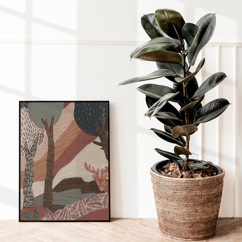 May include: A framed abstract art print with a brown, orange, and blue color scheme depicting a stylized forest scene. The print is hanging on a white wall next to a potted ficus plant with dark green leaves.
