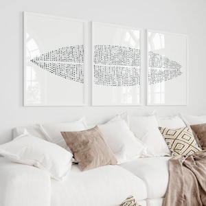 May include: Three white framed prints with a geometric pattern of black dots on a white background. The prints are hanging on a white wall above a white couch with brown throw pillows.