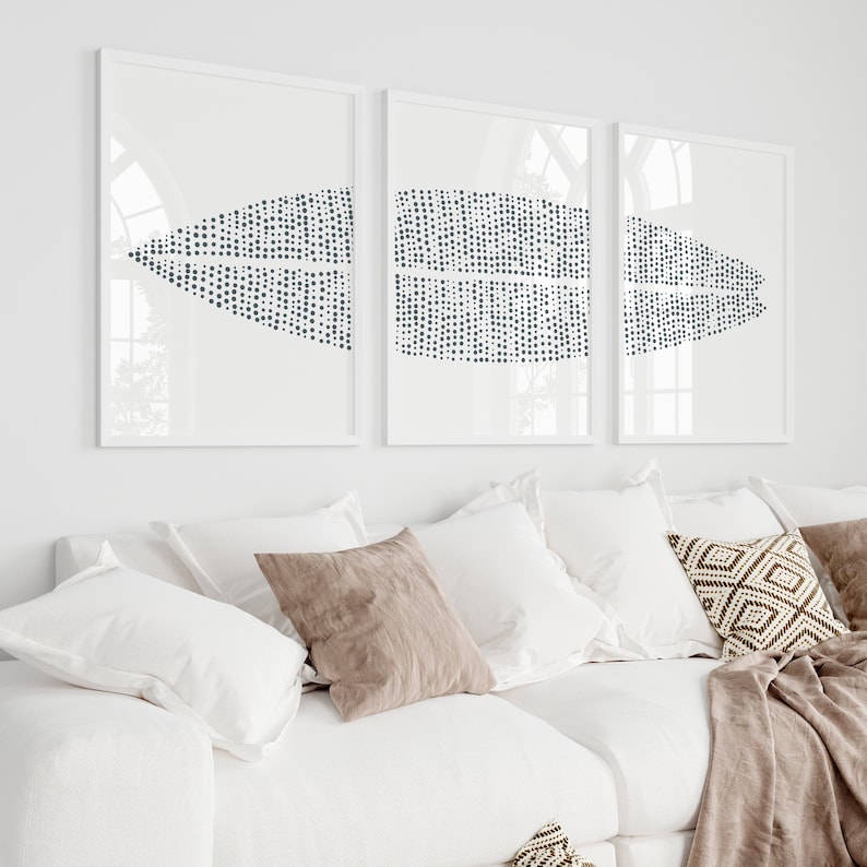 May include: Three white framed prints with a geometric pattern of black dots on a white background. The prints are hanging on a white wall above a white couch with brown throw pillows.