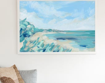 May include: Abstract beach landscape painting in a white frame. The artwork features a light blue sky with white clouds, a sandy beach, and turquoise water. Green and blue brushstrokes depict foliage in the foreground.