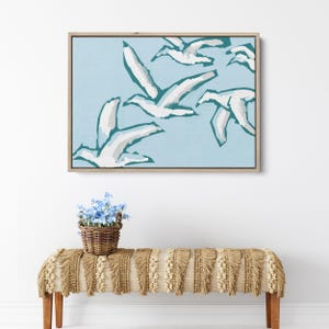 May include: A framed abstract painting of white birds flying in a light blue sky. The birds are stylized and have a teal outline.