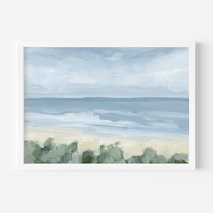 May include: A painting of a seascape with a blue sky, blue ocean, and a sandy beach. The beach is covered in green bushes. The painting is in a white frame.