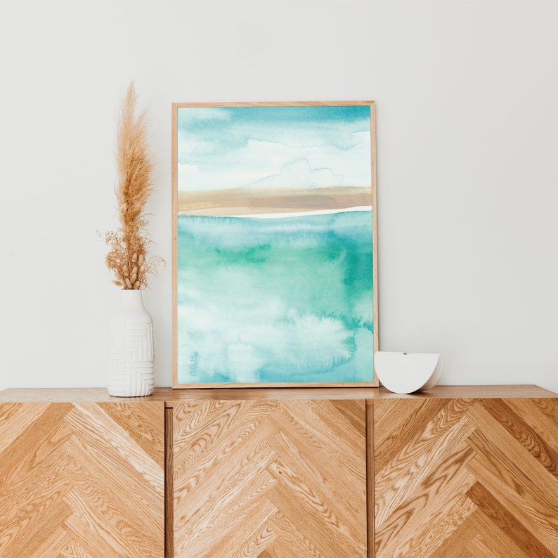 May include: A framed watercolor painting of a seascape with a light blue sky, a thin brown line representing a beach, and a turquoise and green ocean.