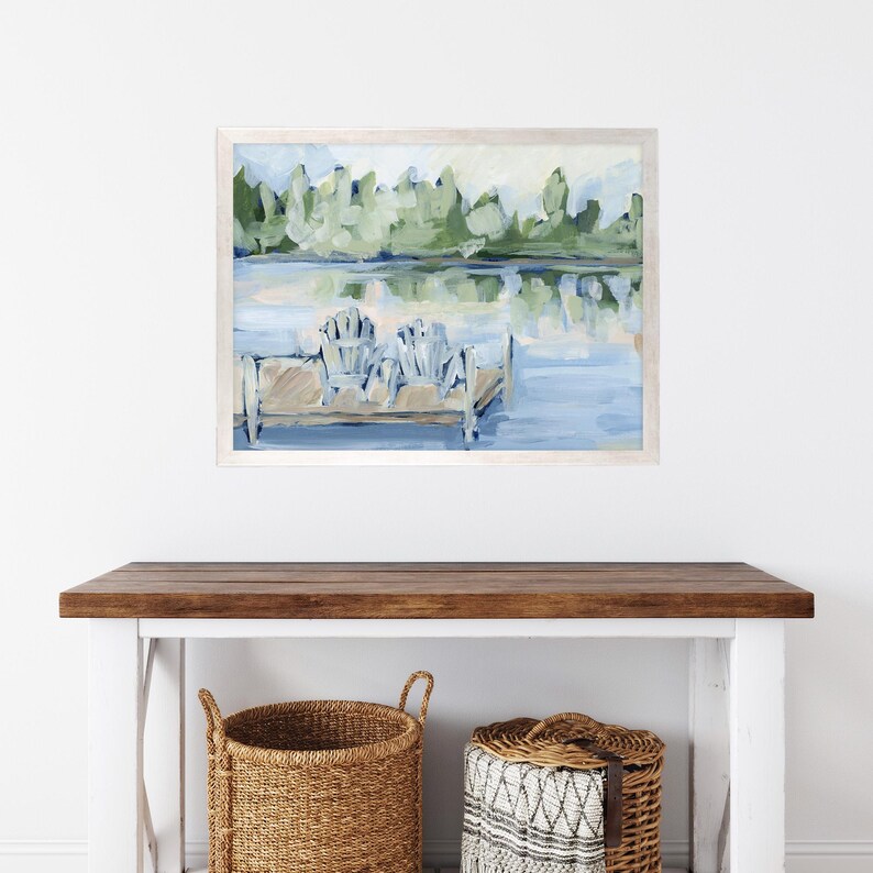 Pode incluir: Uma pintura emoldurada que representa uma cena de lago com duas cadeiras brancas em um cais de madeira. O lago &eacute; azul e as &aacute;rvores s&atilde;o verdes. A pintura est&aacute; em uma moldura branca.
