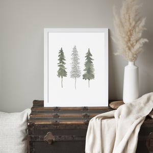 Può includere: Una stampa incorniciata bianca con un'illustrazione ad acquerello di tre alberi verdi su uno sfondo bianco.