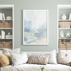 May include: A white framed abstract painting with blue, green, and beige brushstrokes. The painting is hanging on a light green wall above a white couch with pillows.