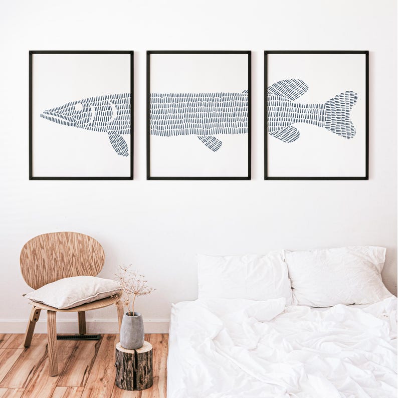 May include: Three black framed prints of a stylized blue fish illustration. The fish is made up of a series of short, thin lines. The prints are hanging on a white wall above a white bed with a wooden headboard.