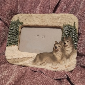 Peut inclure: Un cadre photo rustique avec une scène enneigée et deux loups. Le cadre est fait d'un matériau brun clair qui ressemble à de la pierre. Les loups sont bruns et gris et regardent vers la droite. Le cadre a une ouverture rectangulaire pour une photo.