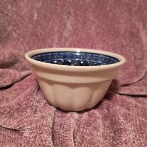 May include: A white ceramic bowl with a blue and green floral pattern around the rim. The bowl has a fluted design and is perfect for serving a variety of dishes.