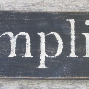 May include: Black wooden sign with white painted lettering that reads "Simplify".
